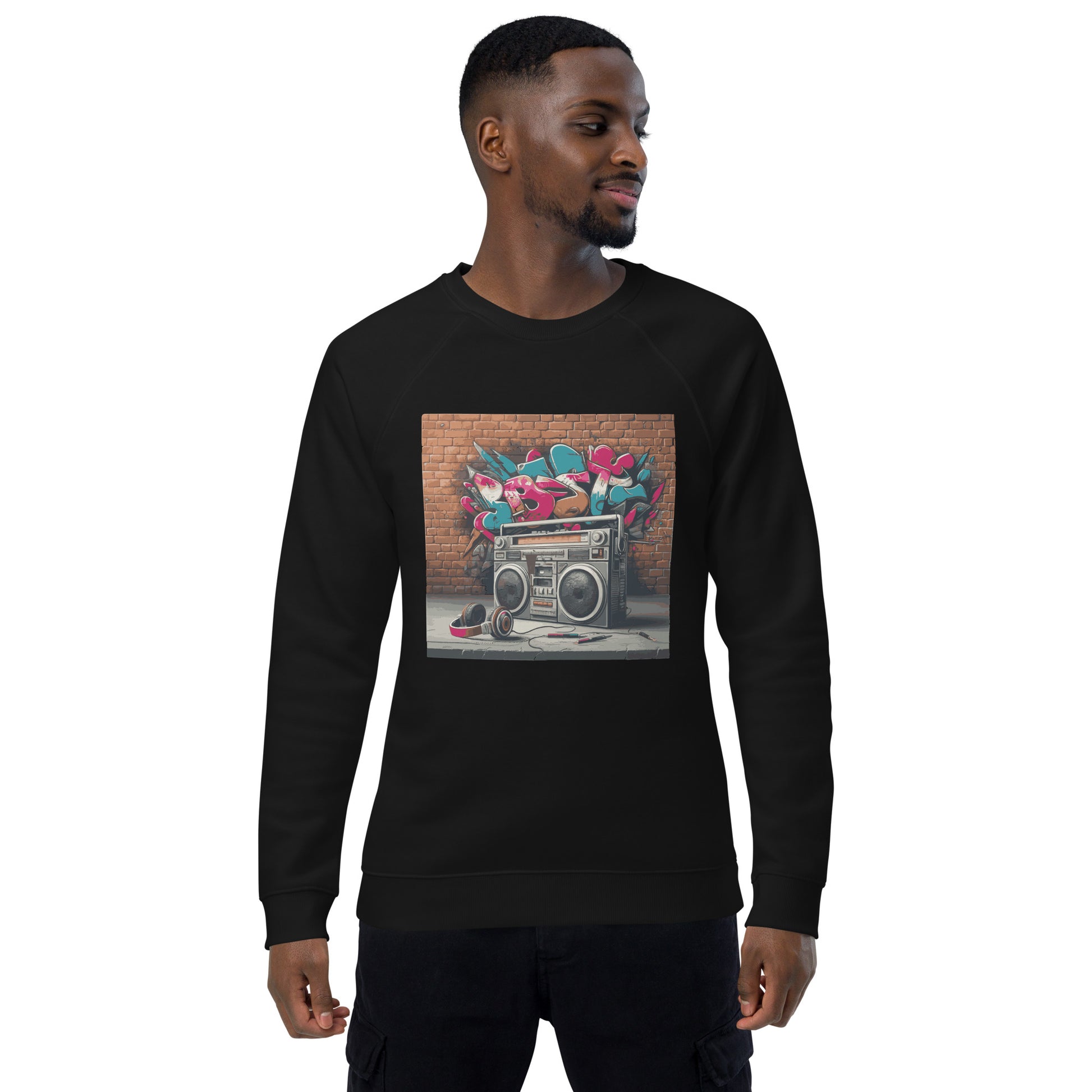 Männliches Model trägt Unisex-Bio-Raglan-Pullover mit Boombox-Design. Schwarze Farbe